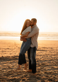 Couple embracing on the beach at sunset during a romantic engagement session by Angie Rich Photography, a San Antonio photographer.