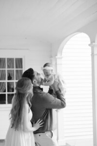 father and mother holding newborn baby up in the air at in-home photography session