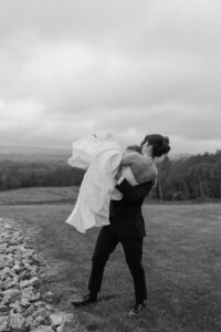 Groom picking up and carrying bride away after wedding in Auburn Maine in black and white.