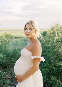 A woman standing with the marsh in the backdrop during her maternity photography session at Wrightsville Beach, North Carolina