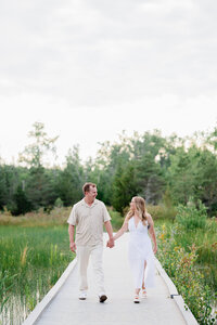 An engaged couple holding hands while walking on a boardwalk during an engagement photography session.