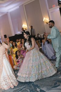 Radiant South Asian bride in pastel floral lehenga laughs joyfully while dancing at her sangeet celebration in a glowing ballroom