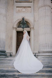 Bride seen from behind in a flowing gown and veil before a grand stone doorway