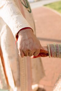 Groom's hand bearing bride's name in mehndi heart clasps her bangle-adorned wrist in warm South Asian wedding detail