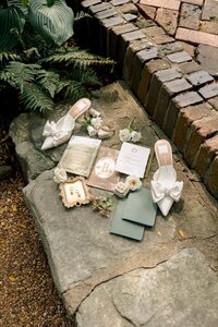 Elegant bridal flat lay with bow heels, invitation suite, jewelry, and florals arranged on rustic stone garden steps