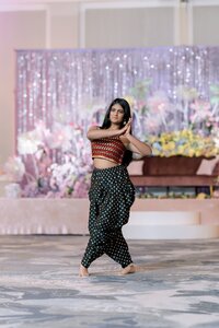 A young woman in traditional South Asian attire performs a graceful dance pose at a glittering Norfolk wedding sangeet celebration