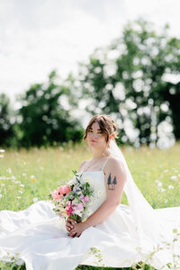 A bride sitting in a field of wildflowers while holding her bouquet during wedding portraits.
