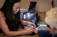 Beauty professional carefully gives an older client a permanent jewelry piece on her wrist.
