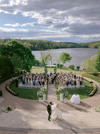 Aerial view of an outdoor lakeside wedding ceremony with guests seated in a circular garden aisle