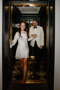 Bride and groom pose together inside a vintage brass and marble elevator