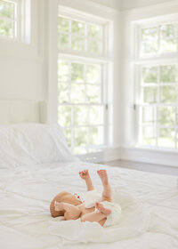A newborn baby boy stretching out on the bed during a newborn photography session in Wilmington, North Carolina