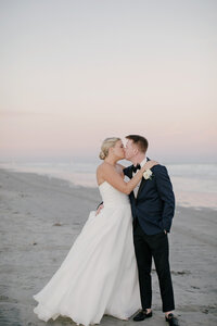 Bride and groom share a kiss on the beach as the sky turns pink at sunset