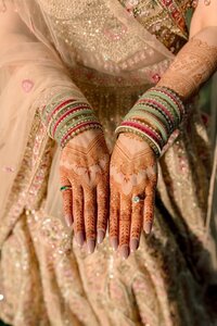 South Asian bride displays intricate henna-covered hands adorned with stacked gold and pink bangles over a glittering champagne lehenga
