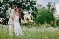 Bride and groom embracing each other while sharing a kiss in a flower field during their wedding portraits.