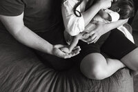 A father holds his newborn sons foot in the palm of his hand during their at home newborn photos in houston tx