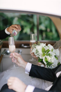 Groom pours champagne into a flute for the bride inside a wedding car