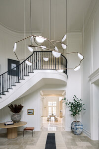 Central, Ohio elegant white entry hall with sweeping staircase, black railings, sculptural pendant lights, potted plants, and a calm, refined atmosphere.