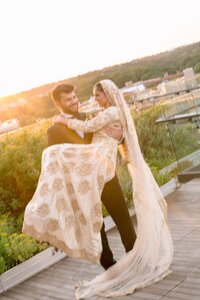 Groom lifts smiling bride in gold embroidered lehenga on a sunlit rooftop terrace at their Washington DC Muslim wedding