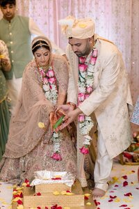 South Asian bride and groom performing a sacred wedding ritual together amid scattered rose petals and floral garlands in Norfolk Virginia