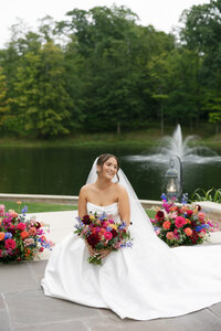 bride sitting in front of her wedding florals on the edge of a pond