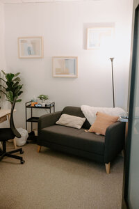 love seat with pillows and blanket that are near a table and chair in therapy office.