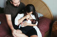 A mother holds her newborn baby and kisses his hand during their at home newborn photos in houston tx