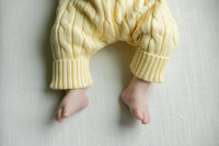 newborn feet wearing yellow sweater pants on a light green backdrop