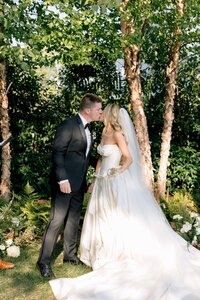 Bride and groom share their first kiss amid lush blue and white floral arrangements at an elegant outdoor garden ceremony