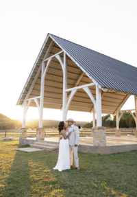 Romantic sunset portrait of a bride and groom embracing beneath a white pavilion at a Texas Hill Country wedding venue, captured with a timeless editorial style by luxury wedding photographer Angie Rich Photography.
