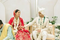 indian-bride-groom-laughing-during-ceremony.jpg indian-bride-groom-laughing-during-ceremony-large.jpg Smiling Indian bride in red lehenga and groom in ivory sherwani share a joyful moment seated together during their traditional wedding ceremony