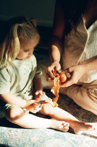 A film photo of a mother peeling an orange for her toddler during her maternity session in her home near houston texas