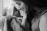 A mother touches her nose to her newborn daughters nose during their at home newborn photos in houston tx