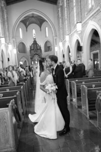 black and white photo of bride and groom standing surrounded by their family in a chapel