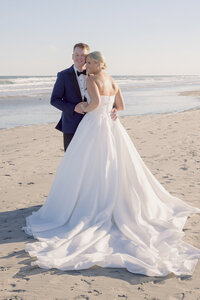 Bride and groom embrace on the beach with ocean waves rolling in behind them