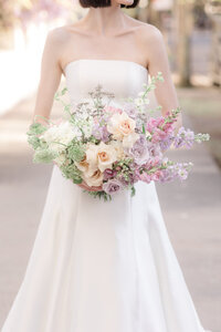 Bride in a strapless wedding gown holding a romantic garden-style bouquet of blush, lavender, and ivory flowers.