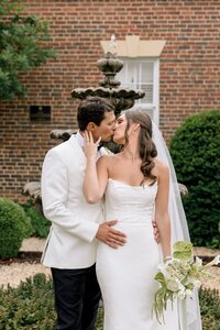 Bride and groom share a tender kiss in front of a stone fountain at Belmont Country Club on a rainy wedding day