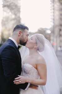 Bride and groom share a kiss on a city street with soft golden light behind them