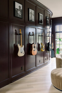 Dark wine-paneled music room displays guitars and framed musician photos, with sunlight streaming through windows for a stylish, inviting feel.