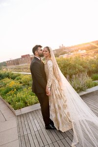 Groom kisses bride's cheek on a sunlit Washington DC rooftop garden as she smiles in a gold-embroidered bridal gown