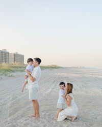 A mom, dad, and two toddler boys playing and laughing on the beach during their sunset family photography session at Wrightsville Beach, North Carolina