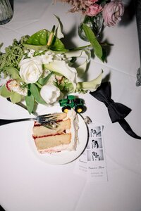 A layered wedding cake slice topped with a toy John Deere tractor sits beside a photo strip and bridal bouquet on a white reception table