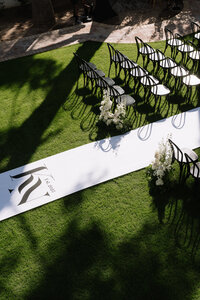 Modern outdoor wedding ceremony with black chairs, white floral arrangements and a custom white aisle runner.