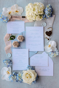 Wedding invitation suite styled with blue hydrangea, orchids, and the couple's rings