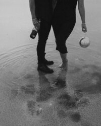 Black-and-white artistic portrait featuring a couple standing in shallow water with cameras and a disco ball by Angie Rich Photography in San Antonio.