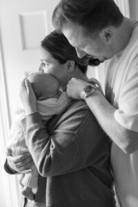 black and white photo of parents looking out a window while holding their baby