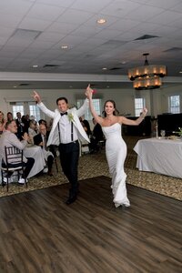 Radiant bride and groom laughing as they make their grand entrance into an intimate reception hall strung with warm fairy lights