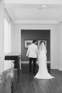 Bride and groom walk hand in hand through an elegant indoor hallway at Belmont Country Club in black and white