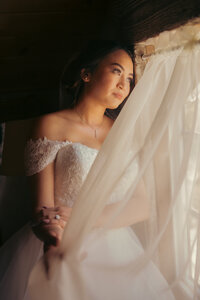 Briding looks through curtain out window- utah wedding photographer