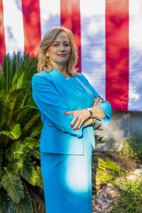 A classic professional portrait taken by Studio Roscher of a female professional smiling in a blue suit in a park with the American flag