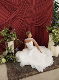 Elegant bridal portrait of a bride in a modern wedding gown seated in front of dramatic red drapery and floral arrangements in San Antonio.